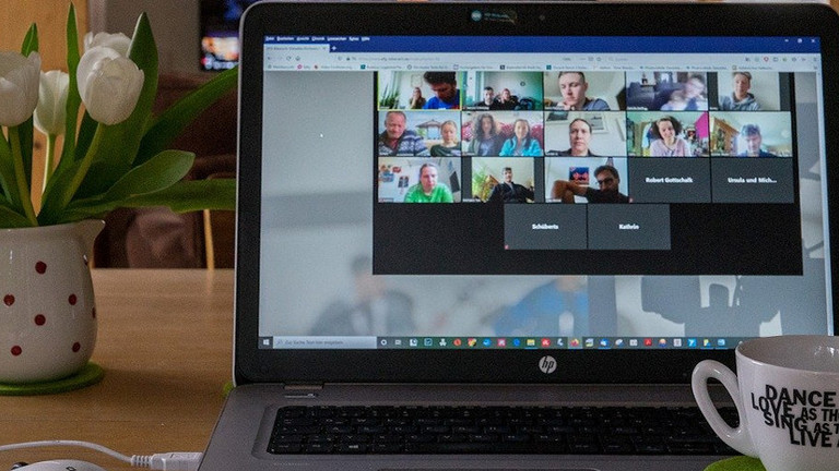 Das Bild zeigt einen Laptop auf einem Tisch. Auf dem Bildschirm ist eine Videokonferenz zu sehen. 