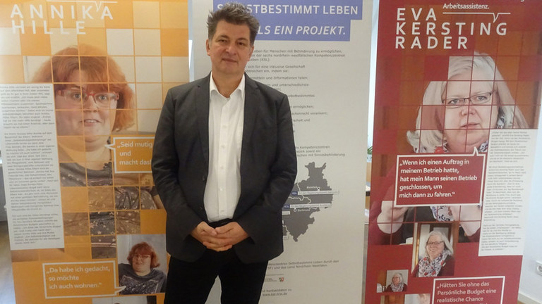 Tobias Fischer, Jurist beim KSL Düsseldorf, steht vor drei Elementen der Ausstellung zum Persönlichen Budget