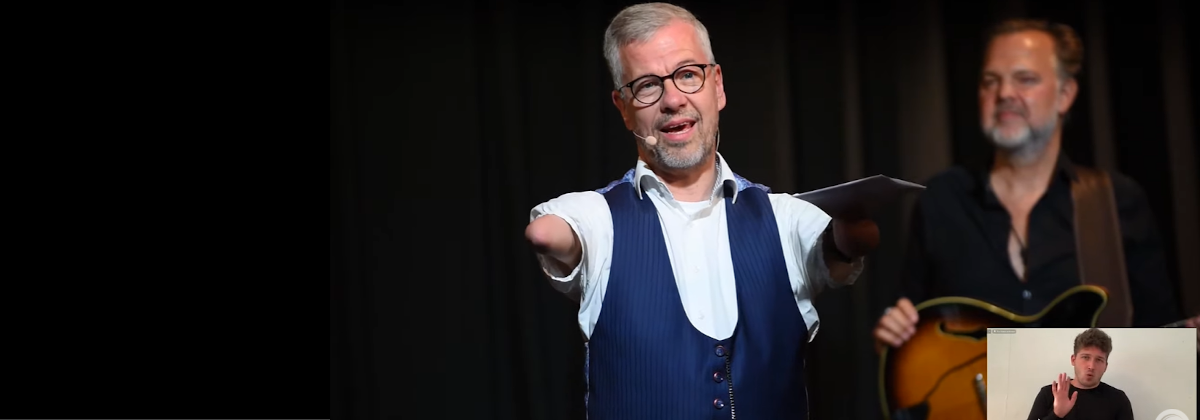 Moderator Rainer Schmidt (links), rechts im Hintergrund: Philipp van Endert mit der E-Gitarre; unten rechts: Gebärdensprachdolmetscher