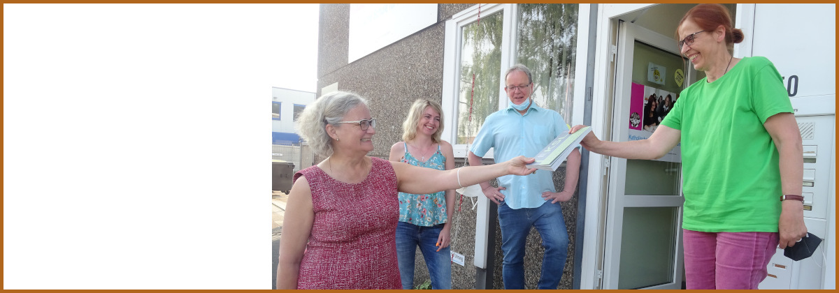 Iris Colsman, Leiterin des KSL Düsseldorf, übergibt das Praxishandbuch an Renate Burmeister-Feldkamp, Leiterin der Katholischen Schule für Pflegeberufe Duisburg e.V.; Im Hintergrund sind zwei Mitarbeiter*innen der Schule.